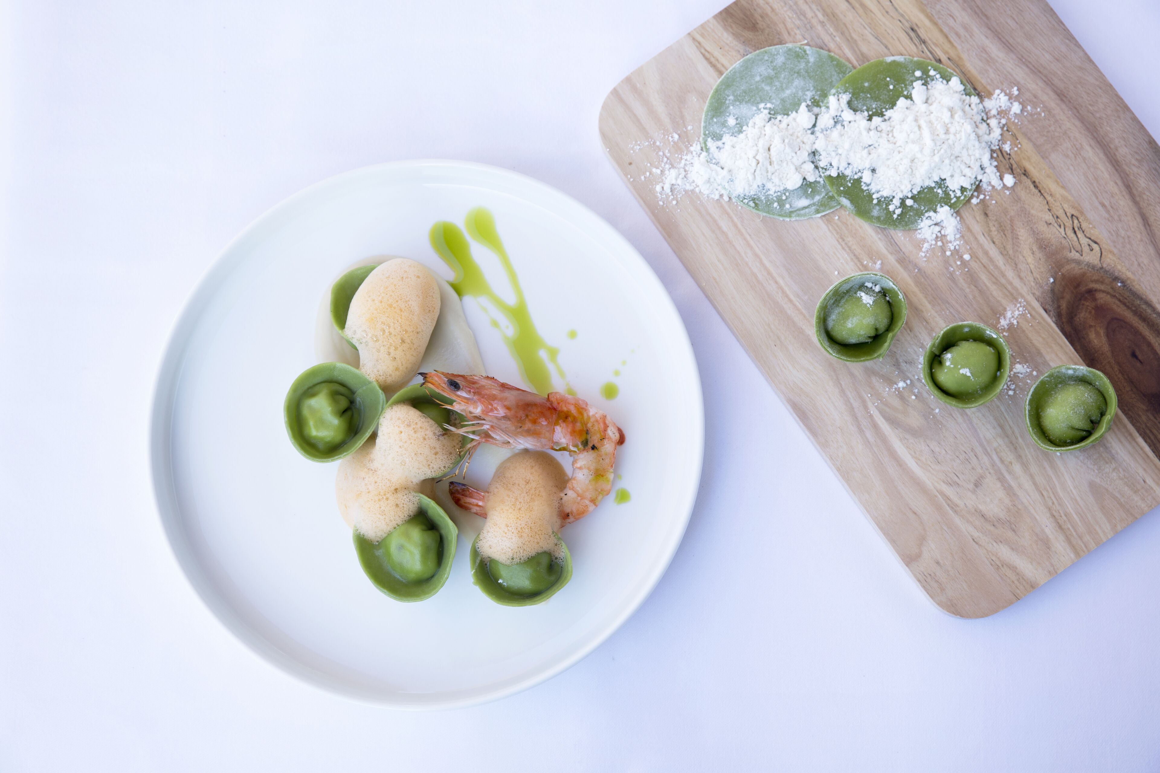 A plate with shrimp and green sauce, and a wooden board with green sauce and salt.