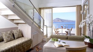 Een moderne hotelkamer met een trap, een bank, een zithoek met uitzicht op zee, en een balkon met een tafel en stoelen.