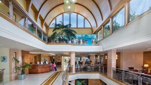 Een ruime hotellobby met een hoge gewelfde plafond, een receptiebalie en een grote plant.