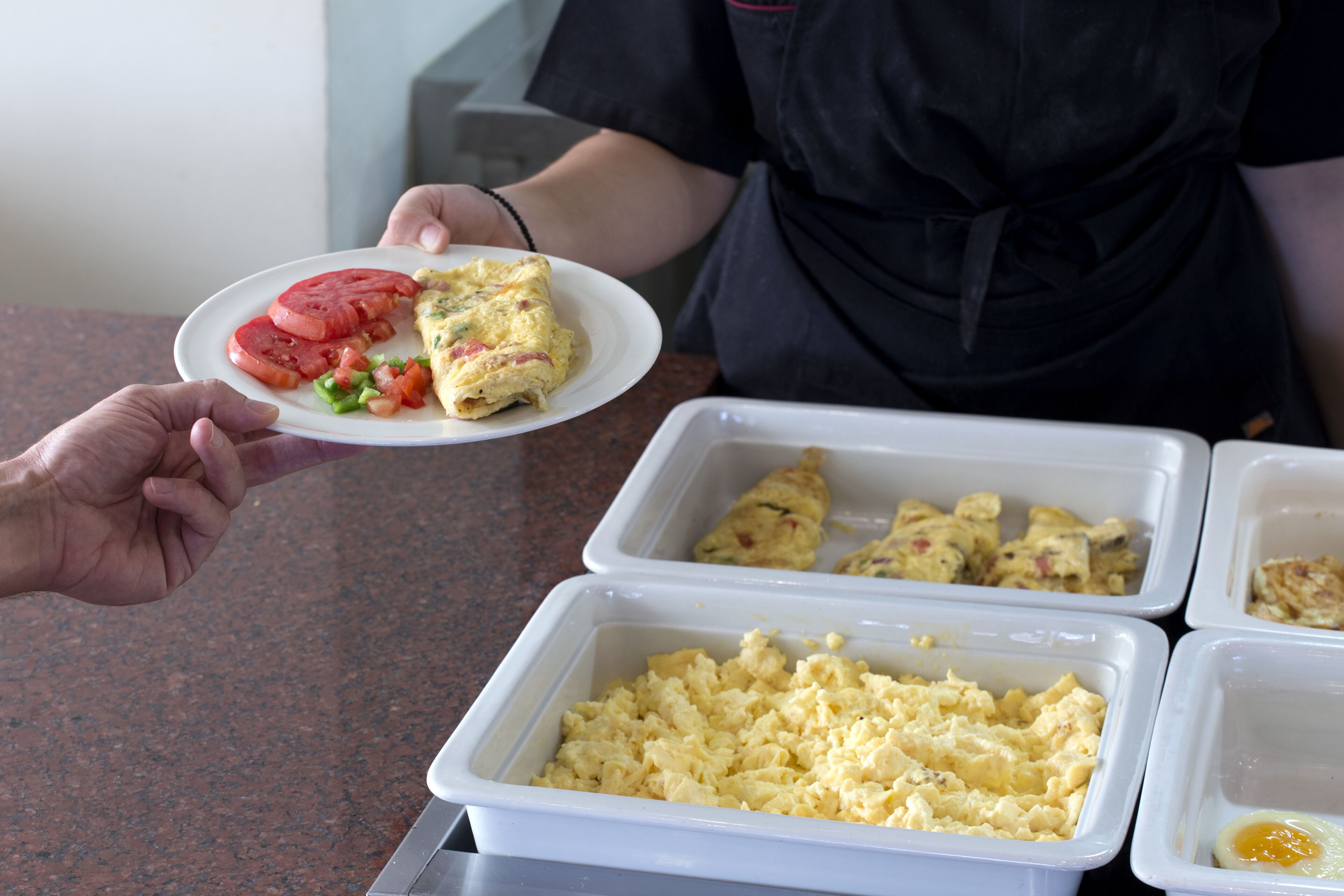 A buffet with scrambled eggs, a slice of tomato, and a rolled omelette on a plate.