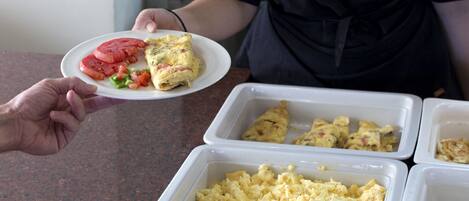 A buffet with scrambled eggs, a slice of tomato, and a rolled omelette on a plate.