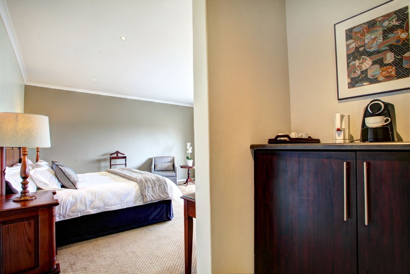 A hotel room with a bed, bedside table, lamp, chair, and a dark wooden wardrobe.