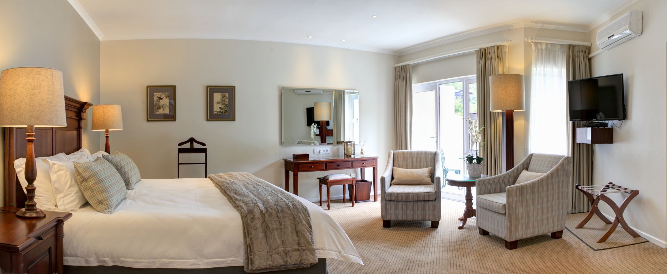 Una habitación de hotel con una cama grande, dos sillones, un escritorio, un televisor y una ventana con cortinas.