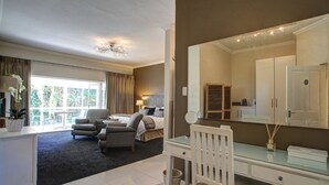 Et moderne hotelværelse med en stor seng, et skrivebord, en stol og et stort spejl. Der er et vindue med gardiner, en plante og udsigt til det frie.