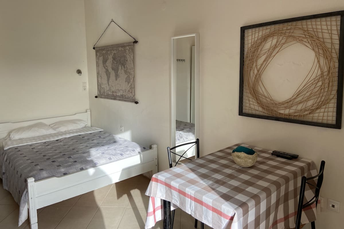 Un dormitorio con una cama, una mesa con mantel a cuadros, una silla, un mapa del mundo colgado y una obra de arte abstracta enmarcada.