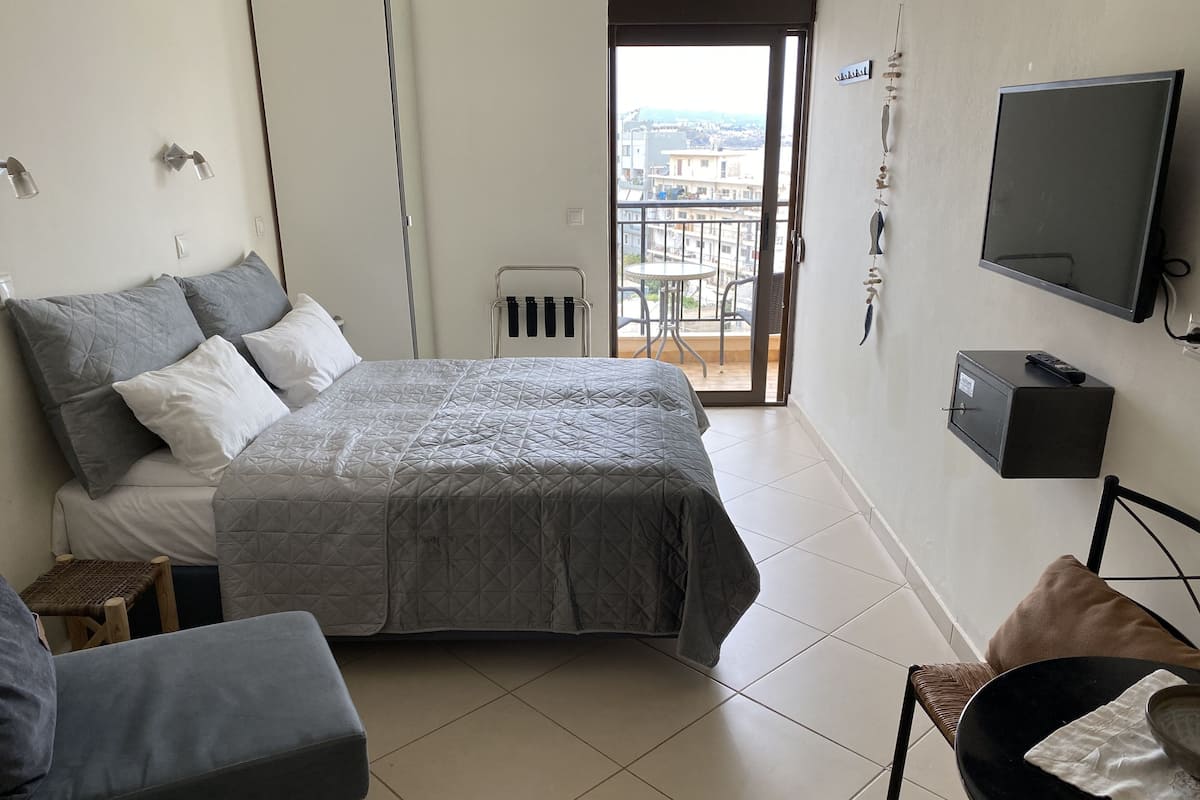 Un dormitorio moderno con una cama grande, una mesita pequeña, una silla y un televisor montado en la pared.