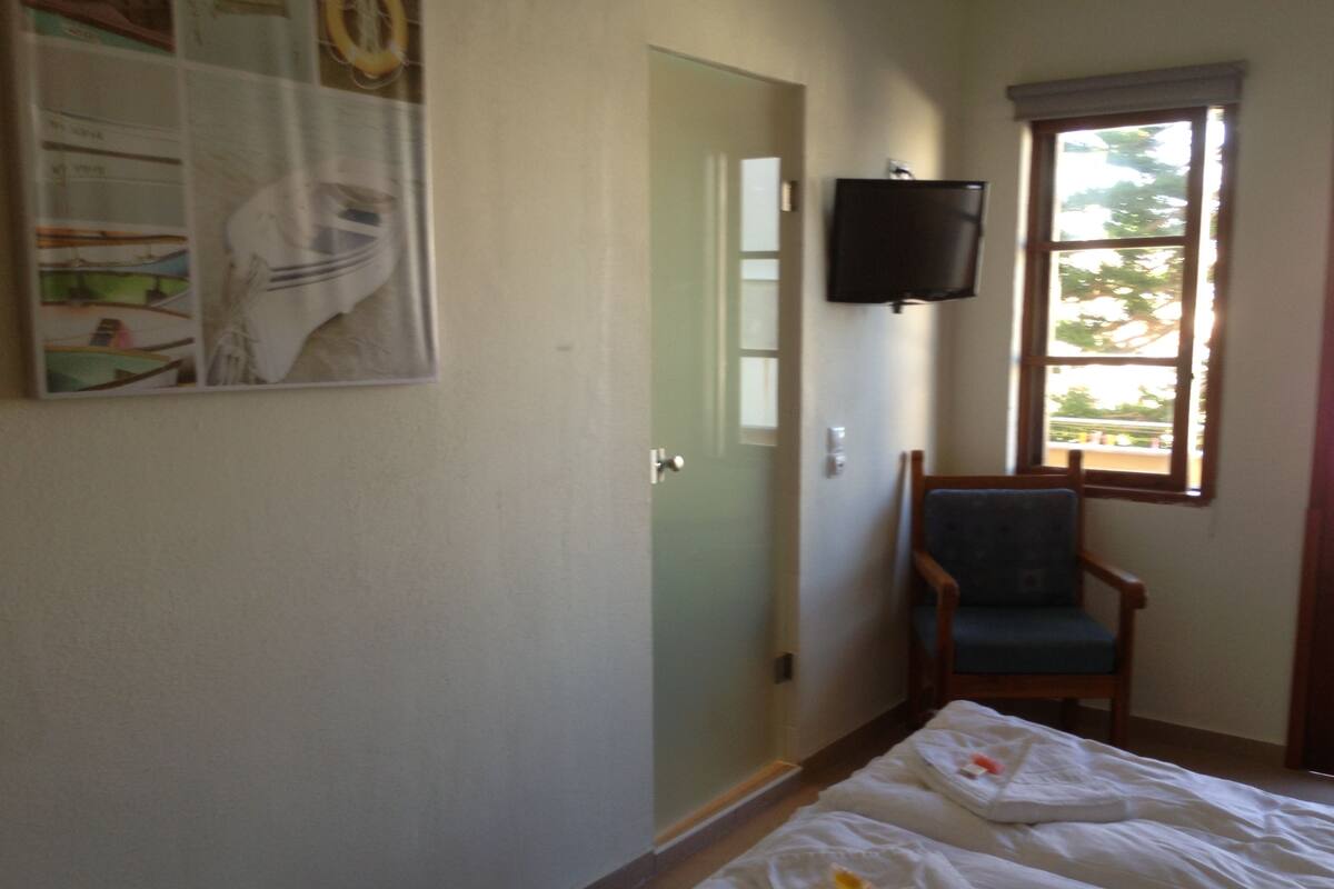 Una habitación con cama, una silla, un televisor y una ventana.