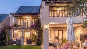 A two-story house with a covered patio area featuring outdoor seating and umbrellas. - Devonvale Golf & Wine Estate (Stellenbosch)