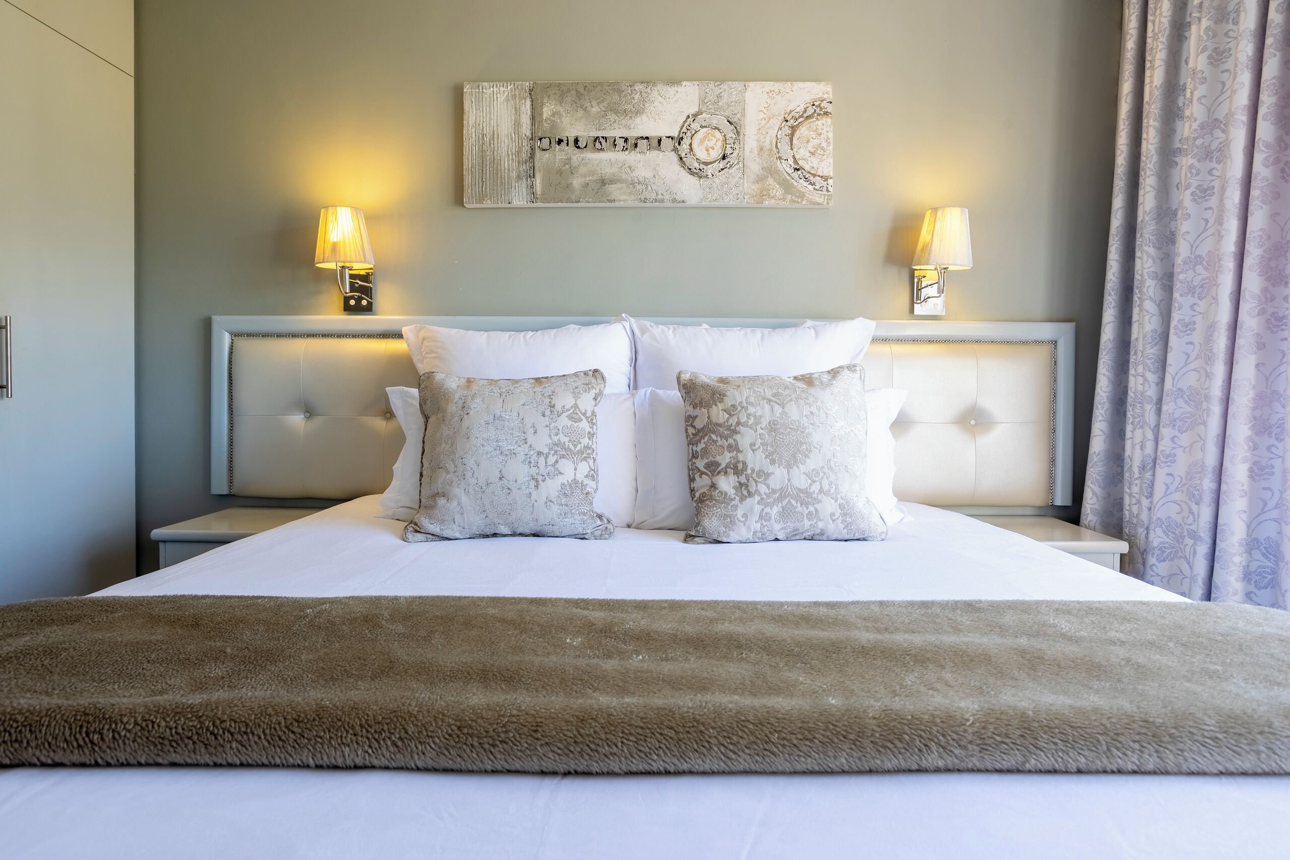 A neatly made bed with a fluffy brown throw, two bedside lamps, and a decorative wall piece above the bed.