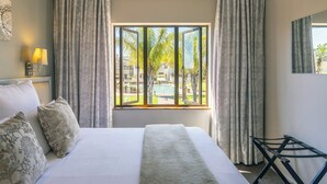 A hotel room with a large bed, a window with curtains, a bedside lamp, and a view of a pool and greenery outside. - Devonvale Golf & Wine Estate (Stellenbosch)