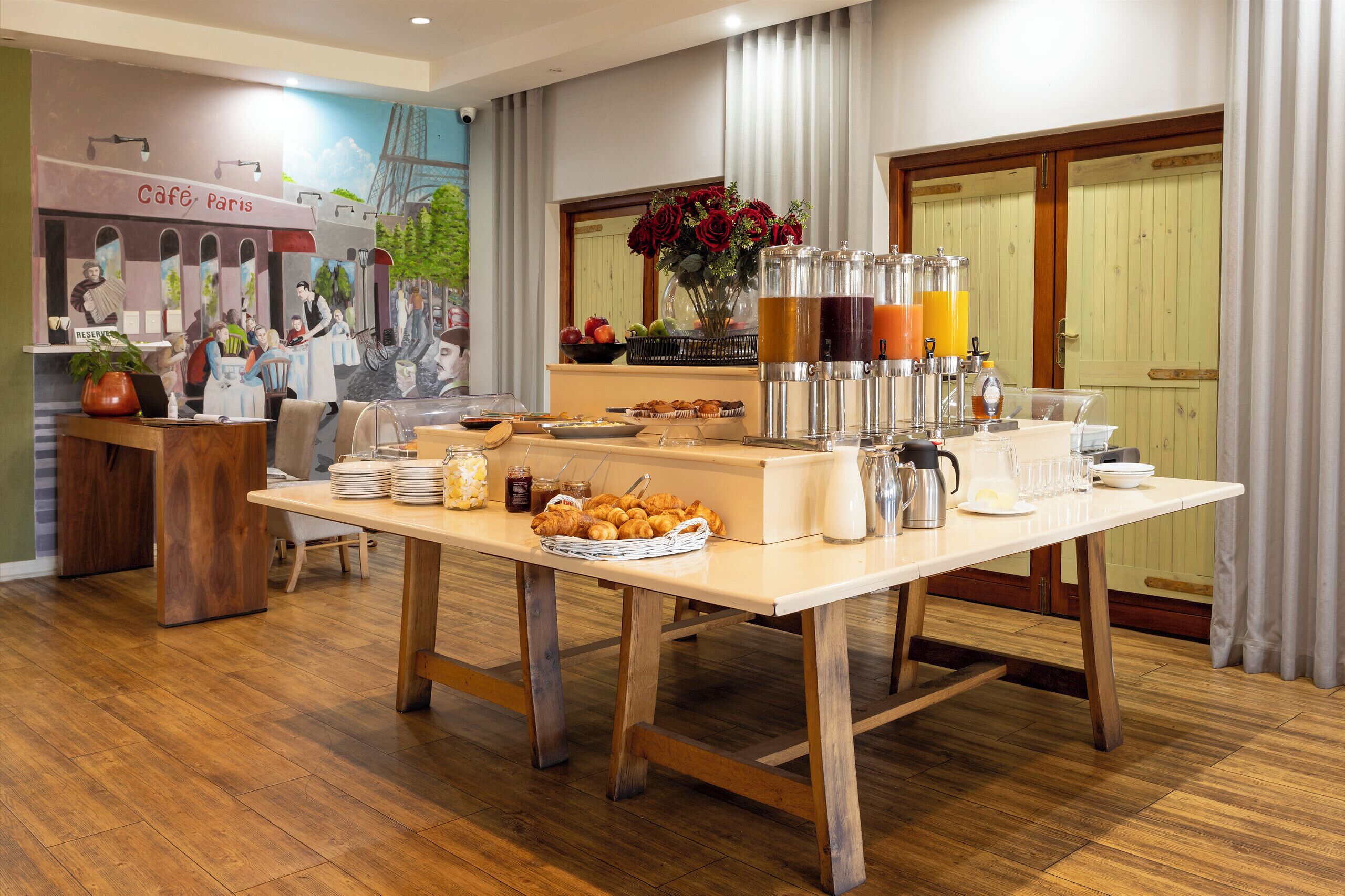 Een ontbijtbuffet met gebak, drankjes en een muurschildering van een café.