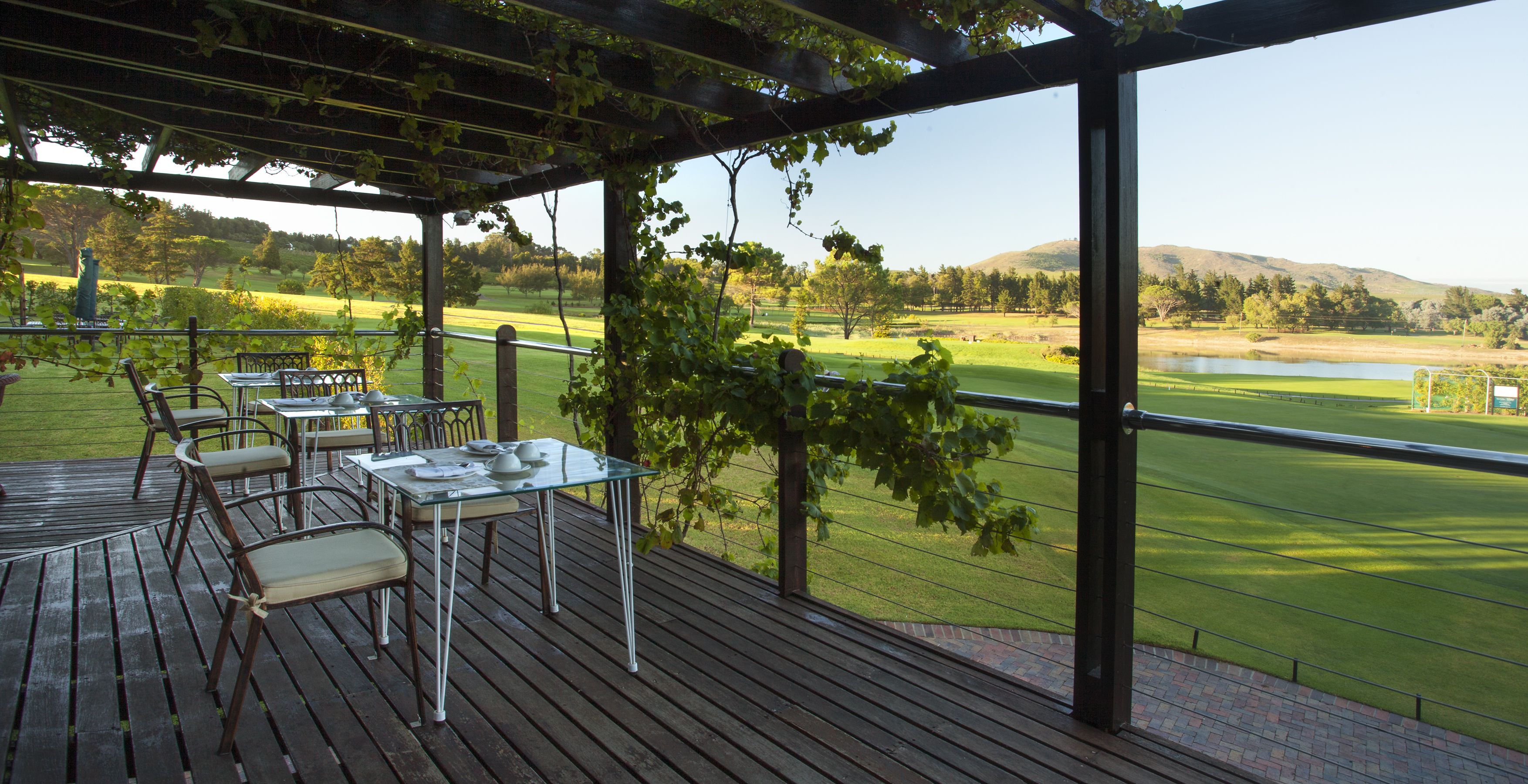 A covered outdoor area with a table and chairs, overlooking a golf course.
