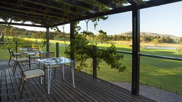 A covered outdoor area with a table and chairs, overlooking a golf course.