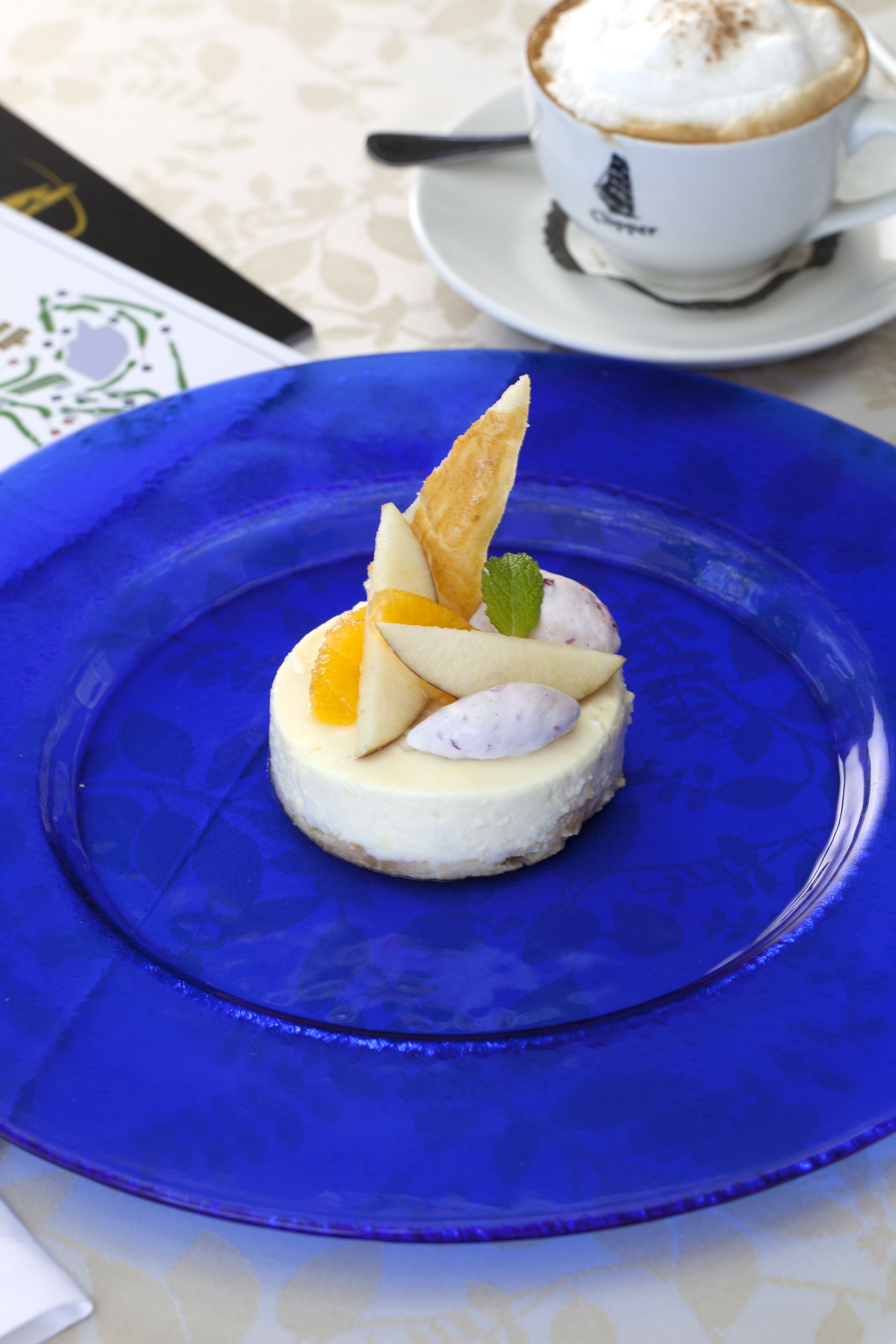 Un postre en un plato azul, con una taza de café al fondo.