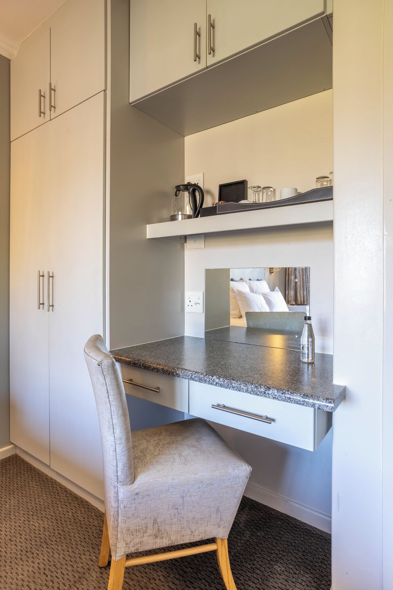 A modern kitchen with white cabinets, a granite countertop, and a grey upholstered chair.