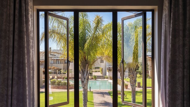 A window with a view of a well-maintained garden, including trees and a swimming pool. - Devonvale Golf & Wine Estate (Stellenbosch)