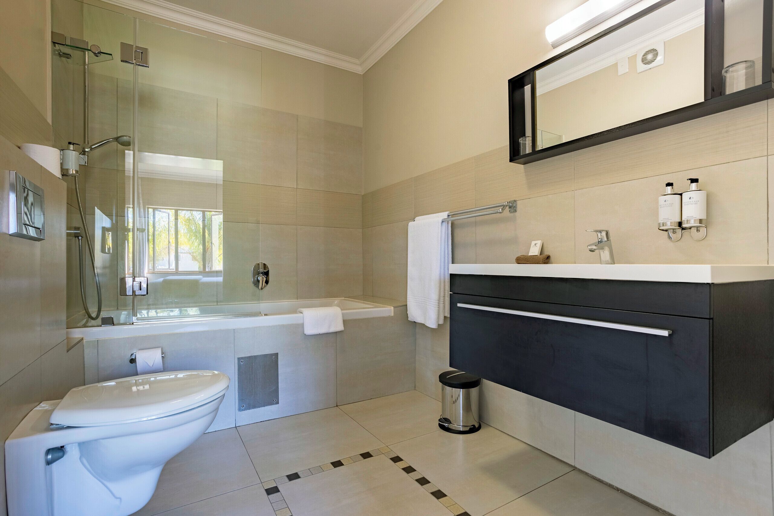 Un baño moderno con ducha envuelta en vidrio, inodoro blanco, bañera y tocador con espejo.