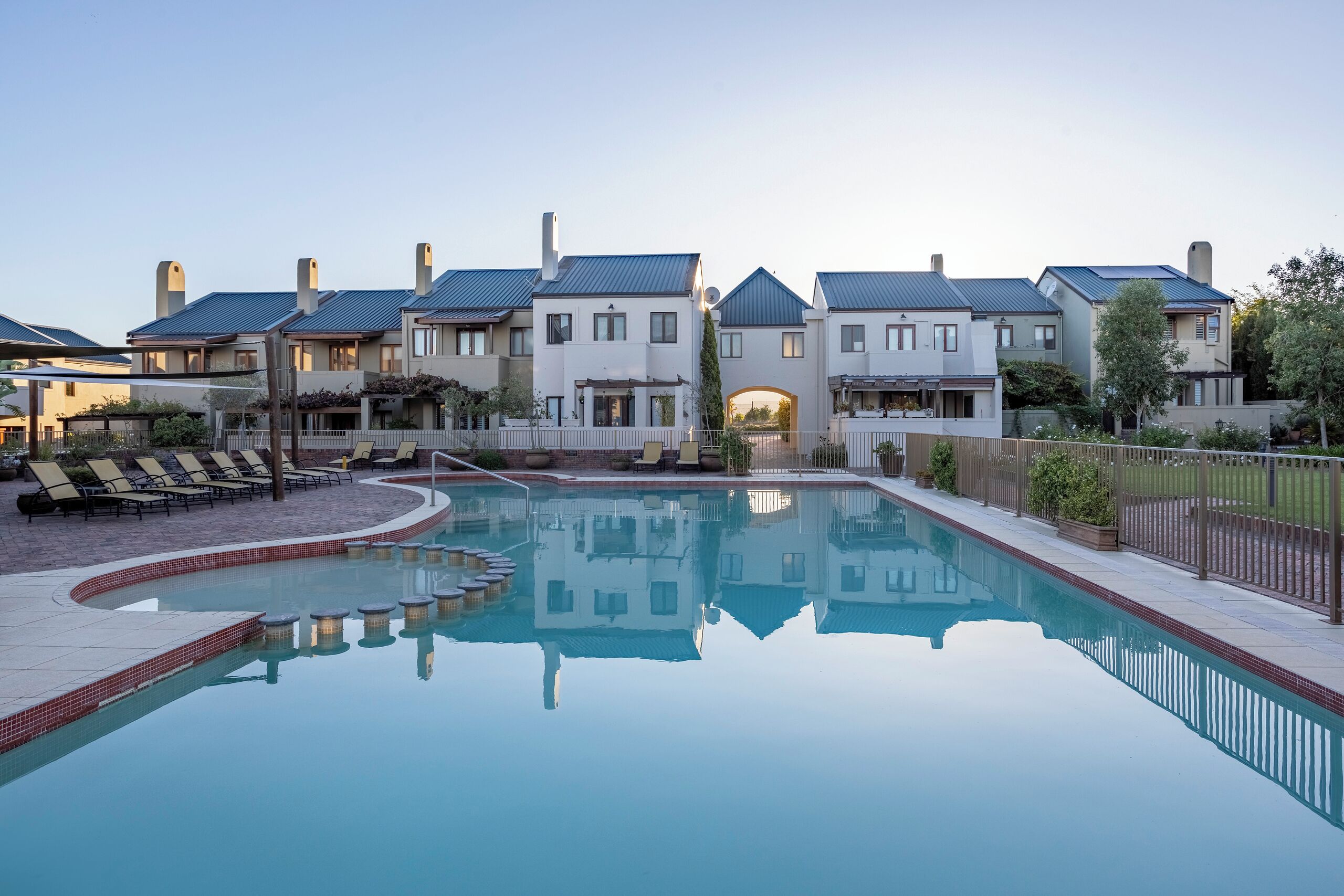 Un complejo residencial moderno con piscina central, sillas de descanso y un jardín bien cuidado.