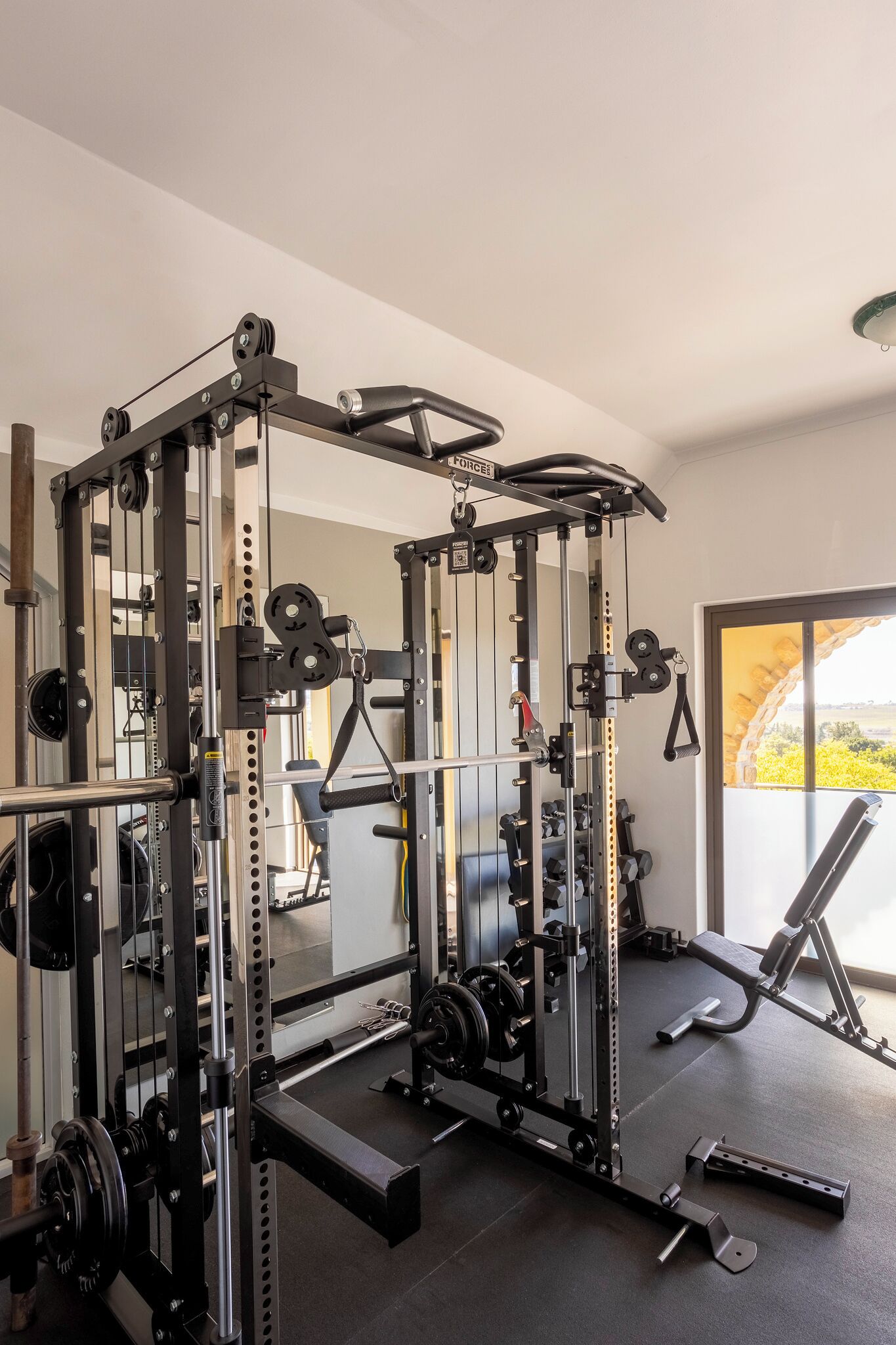 A gym with a squat rack, weight bench, and various free weights.