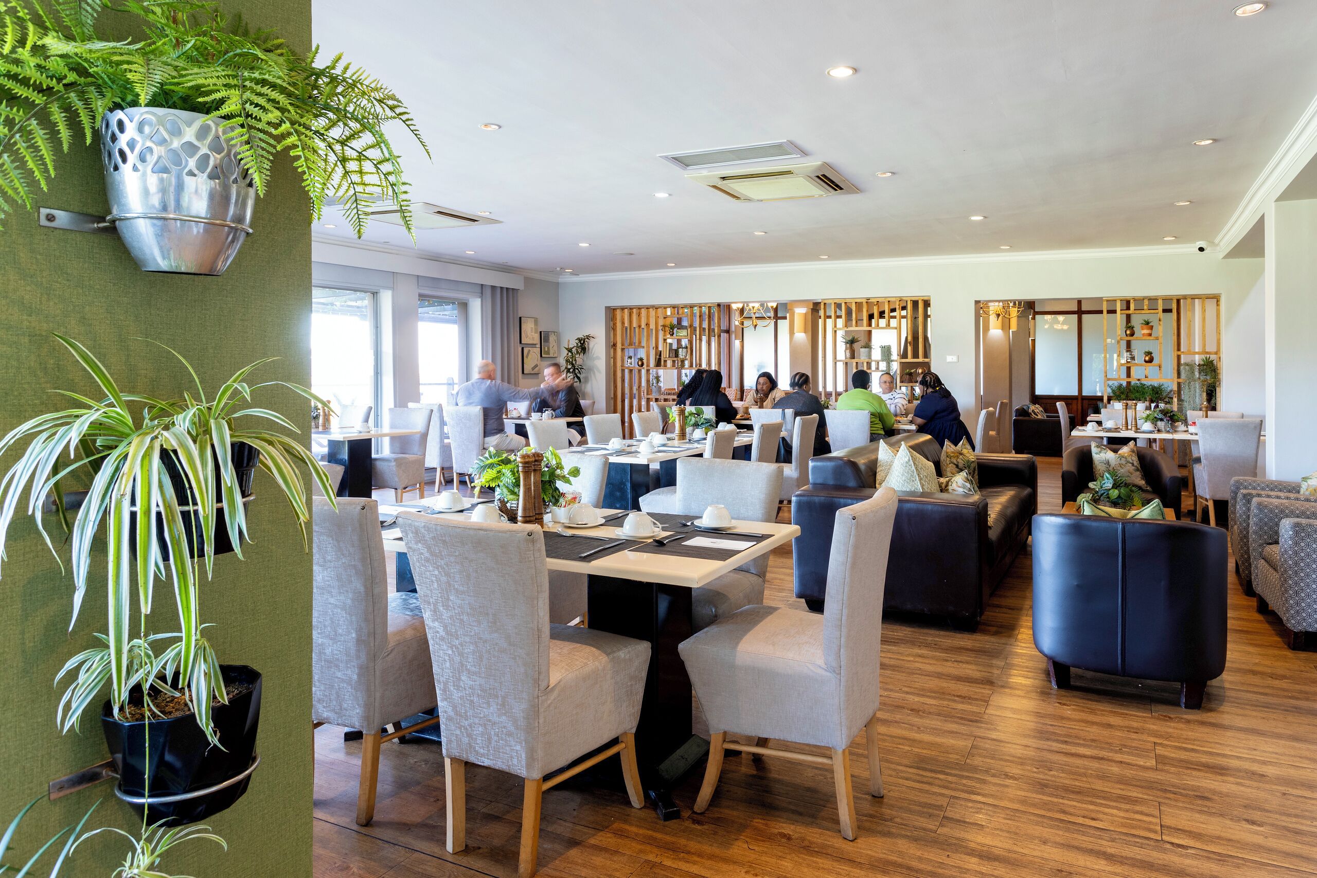 A modern restaurant with indoor seating, potted plants, and a wooden floor.