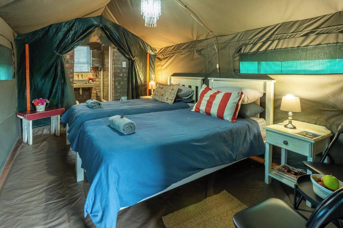 A tented room with two beds, a small table with a lamp, and a chair.