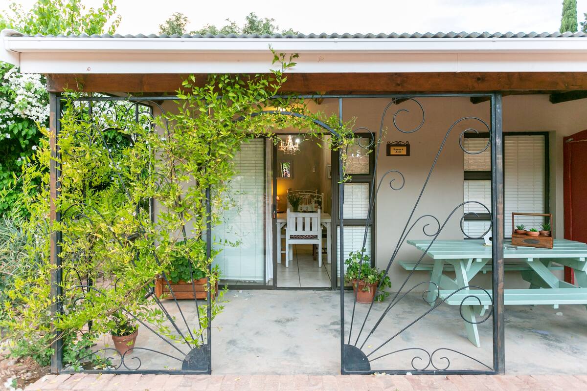 A covered patio with a table and chairs, potted plants, and a door leading to an interior space.