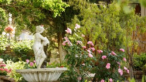 A garden with a stone fountain, lush greenery, and pink flowering plants. - Die Fonteine Guesthouse and Glamping (Oudtshoorn)