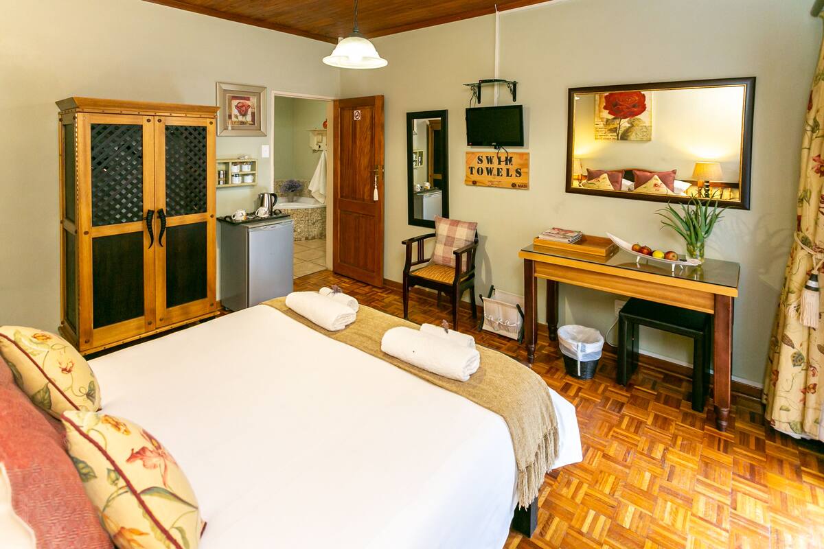 A hotel room with a bed, a desk with a chair, a wardrobe, a mirror, and a television.