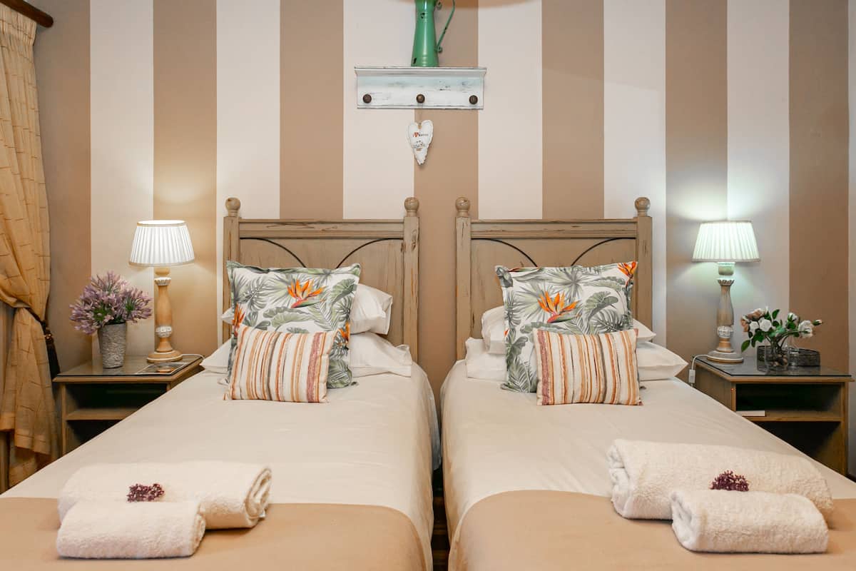 A hotel room with two beds, each with matching floral pillows and towels. There are bedside tables with lamps and decorative items.