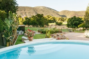 A swimming pool with a view of a landscaped garden, a wooden deck, and a mountain in the background. - Die Fonteine Guesthouse and Glamping (Oudtshoorn)