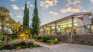 Enjoy the serene atmosphere of our outdoor space, featuring a covered patio with a view of the interior, surrounded by lush plants and a stone wall.