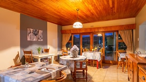 A dining area with wooden ceiling, tables with tablecloths, chairs, and a chandelier. - Die Fonteine Guesthouse and Glamping (Oudtshoorn)