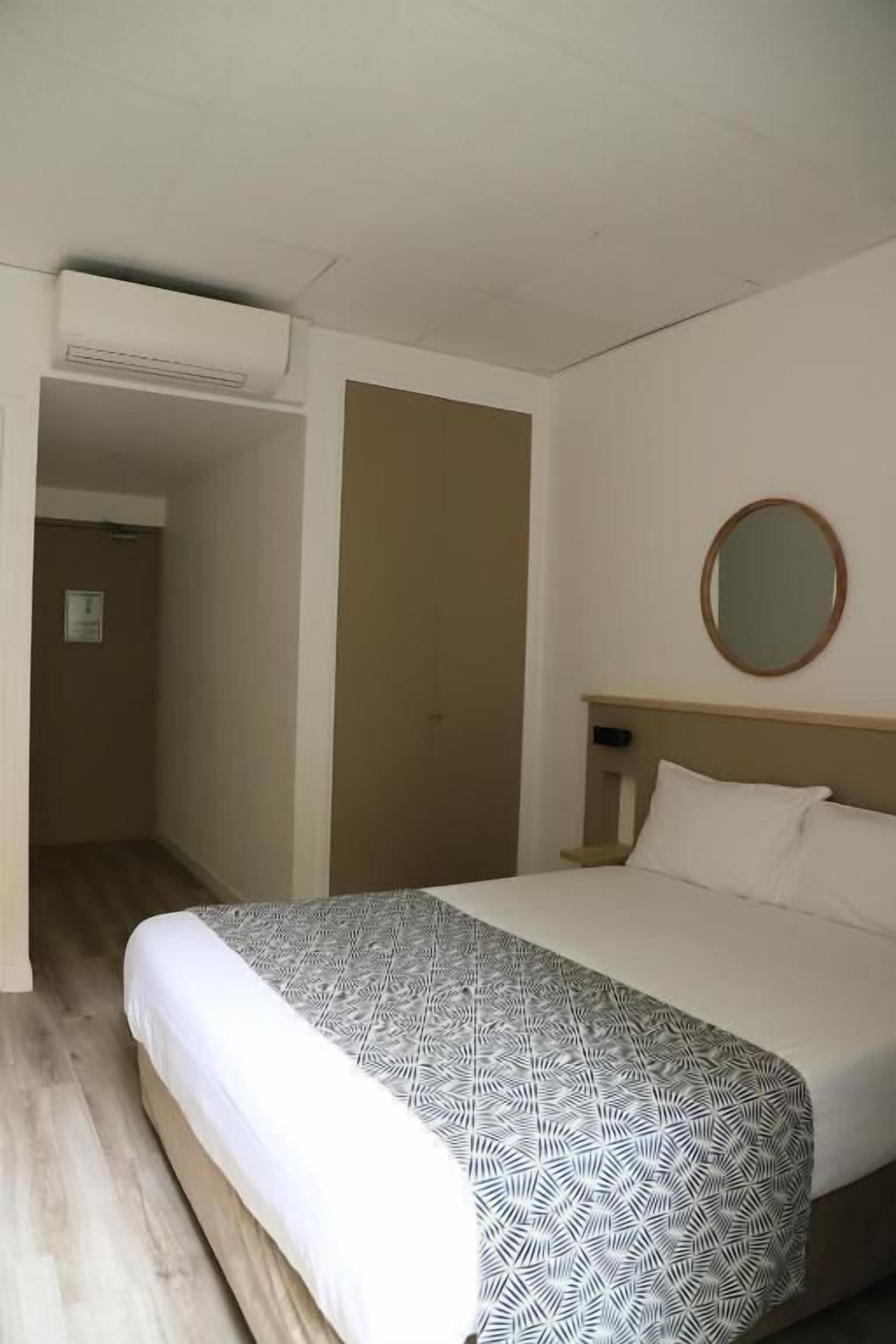 A hotel room with a bed, a round mirror, and a wooden floor.
