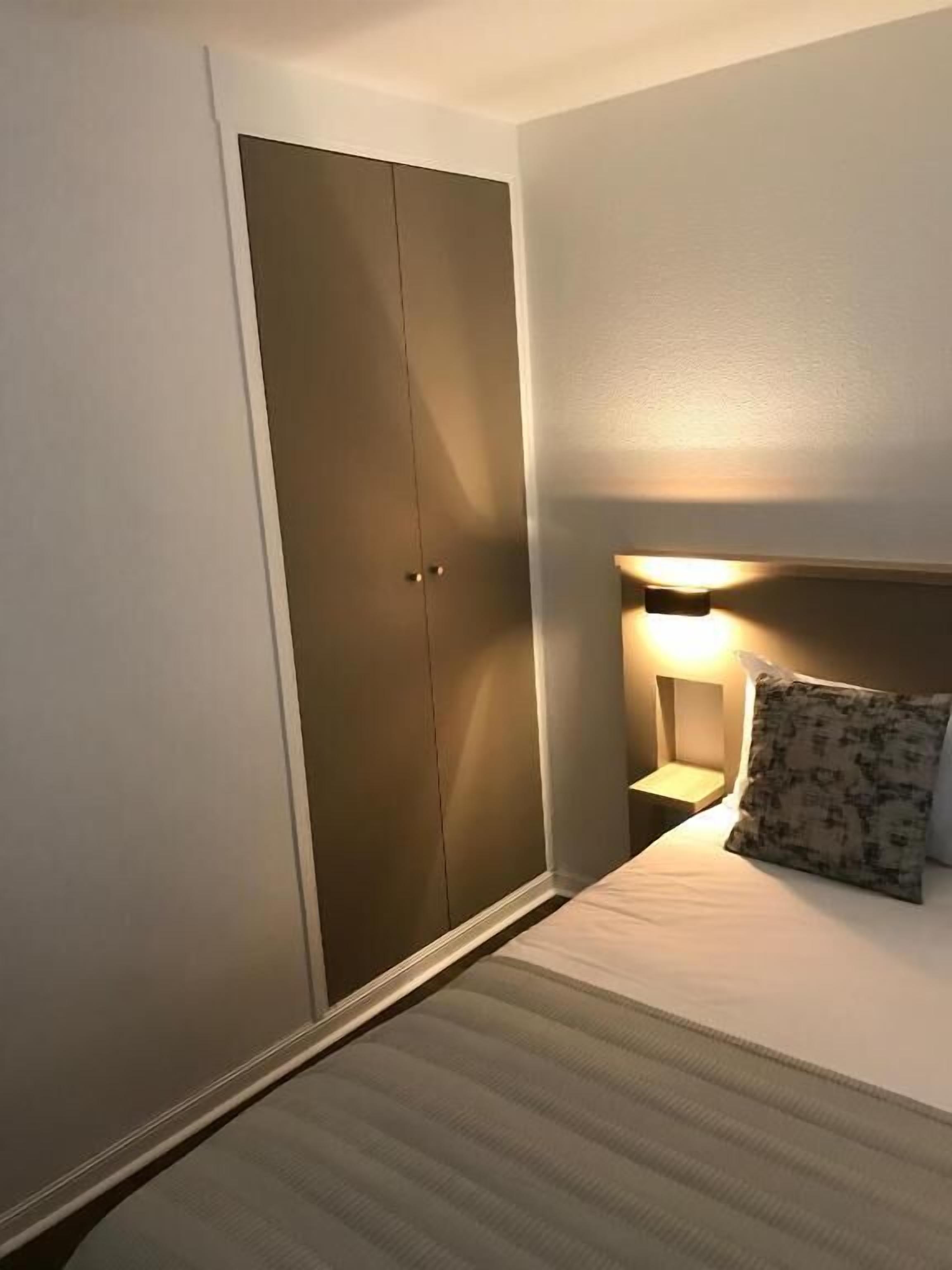 Et hotelværelse med en seng, et natbord med en lampe og et klædeskab.