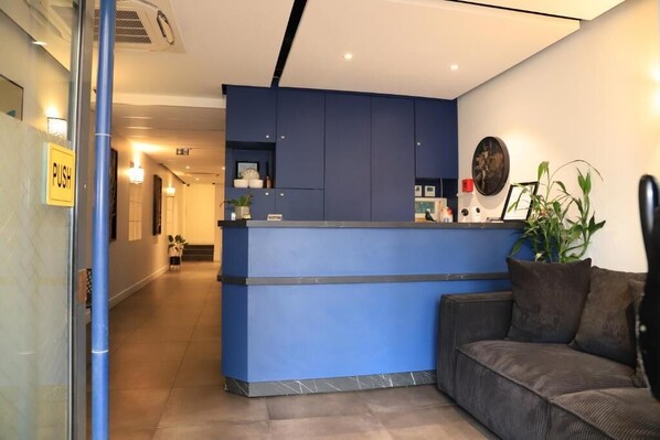 A reception area with a blue counter, a sofa, and a potted plant. - AMHotel (Paris)