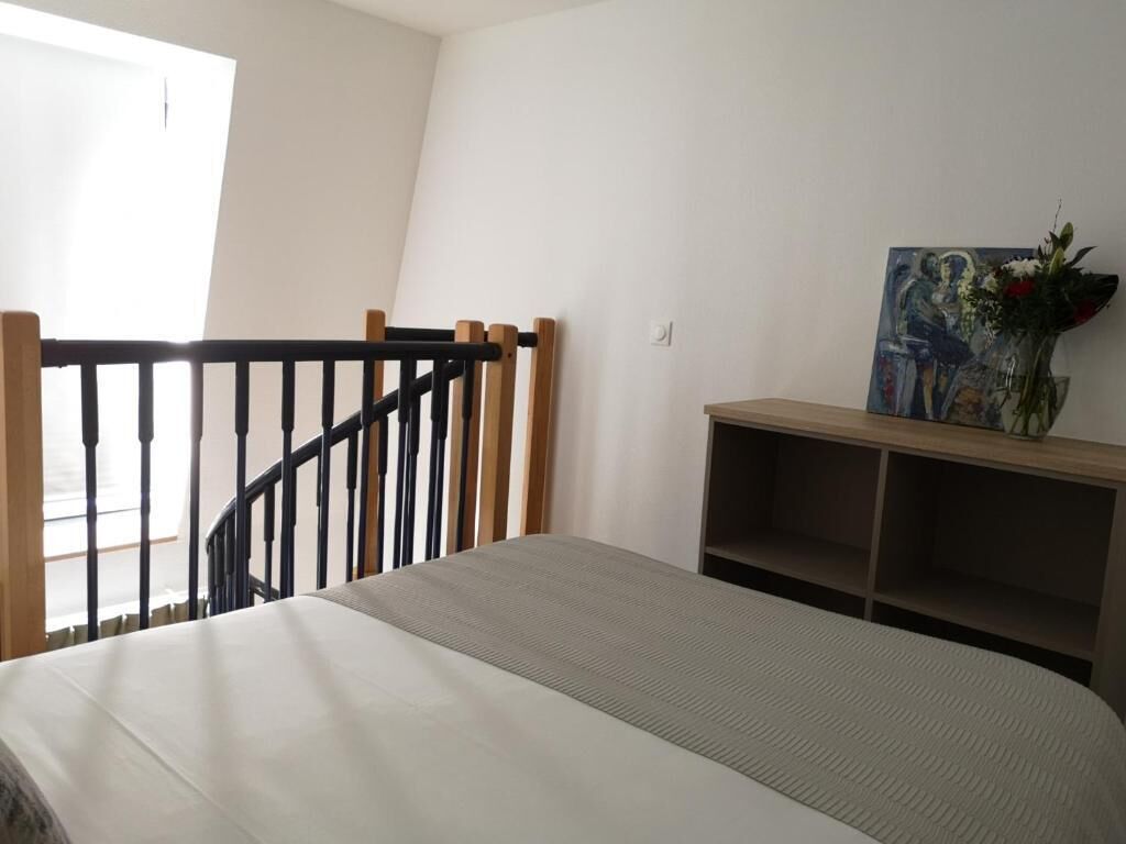 Un dormitorio con una cama, barandal de madera, un cuadro y un jarrón con flores.