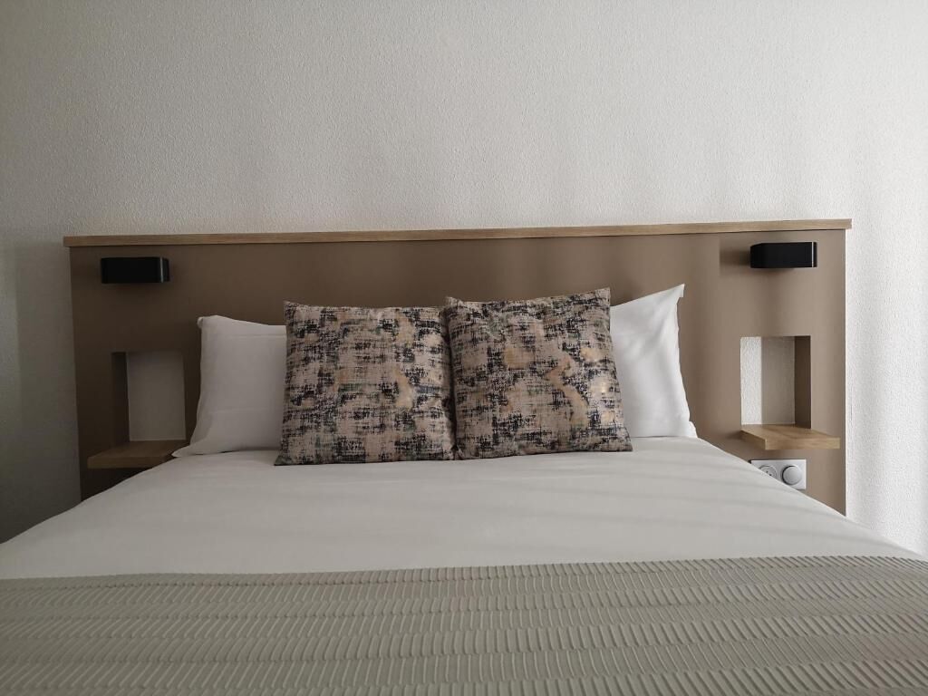 Cama bem arrumada com um travesseiro estampado, um travesseiro liso e uma mesa de cabeceira com abajur.