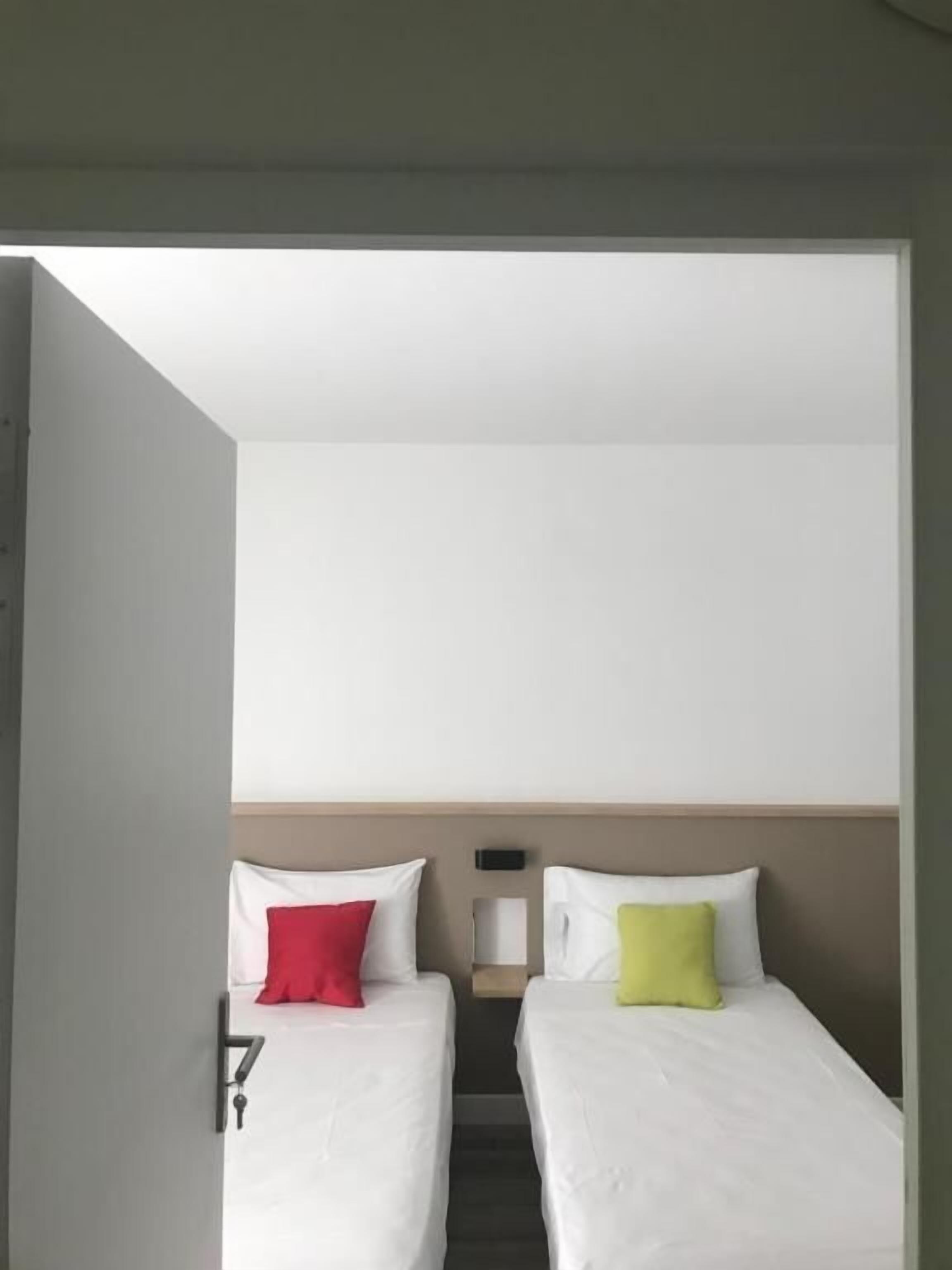 A hotel room with two beds, each with a pillow, a small table, and a wall-mounted device.
