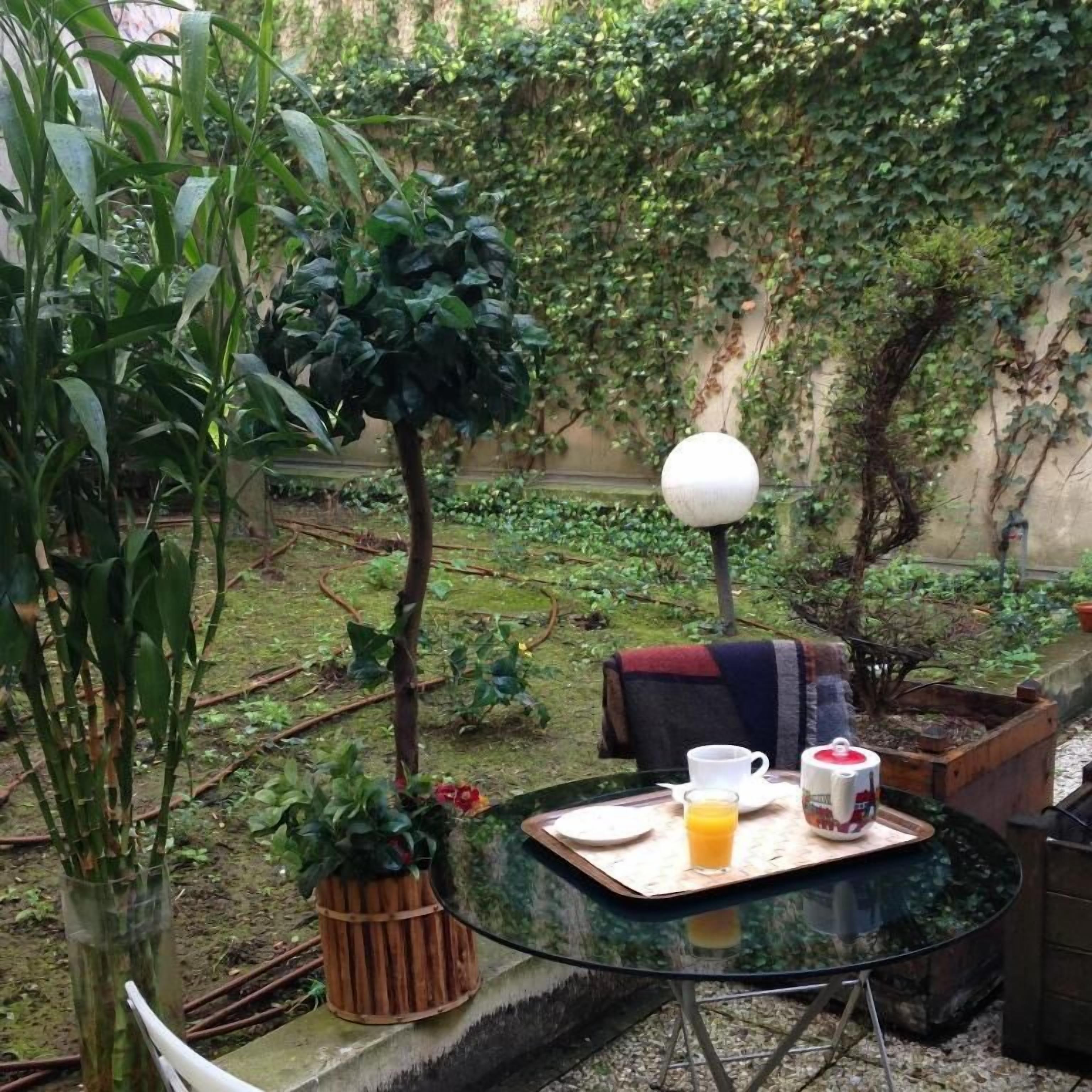 A glass table with a tray of breakfast items, a chair, and a lamp in a garden setting.