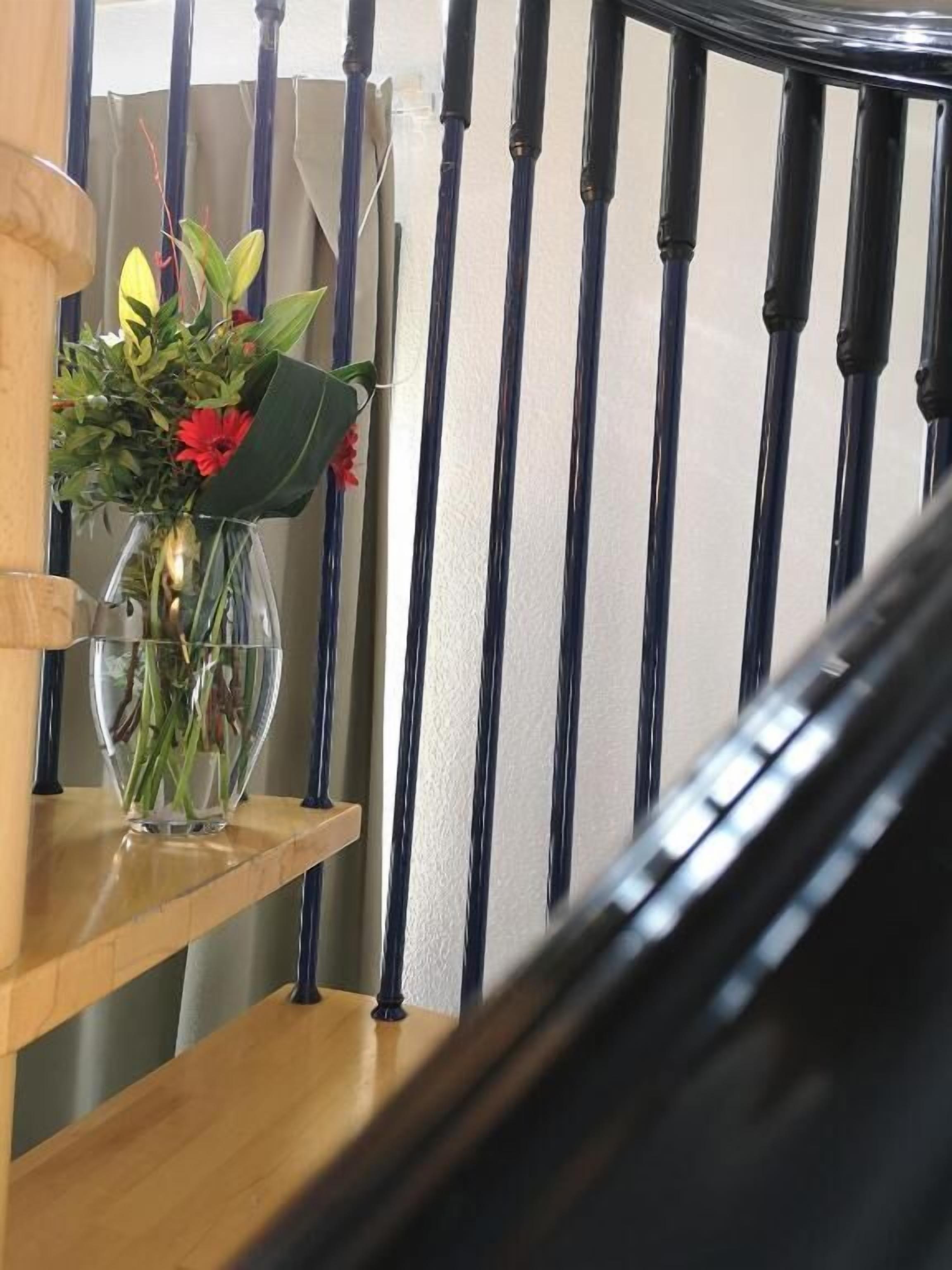 A staircase with a wooden handrail and a clear glass vase with flowers on a shelf.