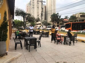 An outdoor cafe with tables and chairs, a waiter, and a bus in the background.