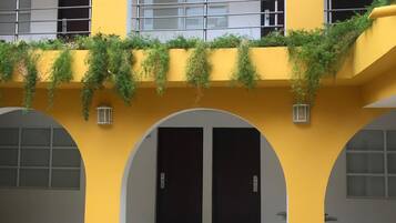 Un bâtiment à la façade jaune, doté de plusieurs portes en arc de cercle et d’un balcon orné de plantes.