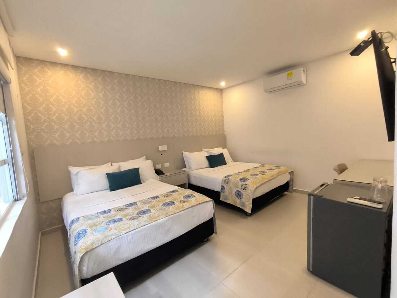 Una habitació d'hotel amb dos llits, un escriptori, una làmpada i un aparell d'aire condicionat.