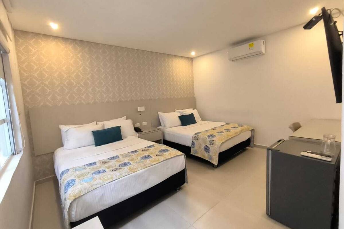 Ein Hotelzimmer mit zwei Betten, einem Schreibtisch, einer Lampe und einer Klimaanlage.