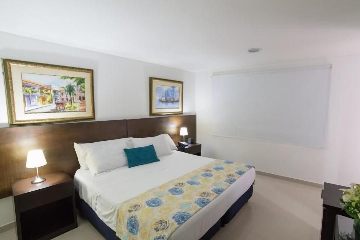 A hotel room with a bed, two bedside tables, a TV, and two framed pictures on the wall.