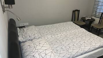 Una cama bien tendida con una colcha de estampado geométrico, una mesita de noche con lámpara y una silla en una zona adyacente.