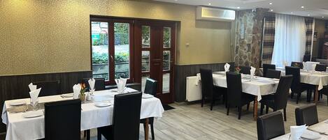 A restaurant with multiple tables set for dining, featuring a stone wall and wooden flooring.
