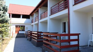 A multi-story building with a red-tiled roof, balconies with wooden railings, and a paved walkway.