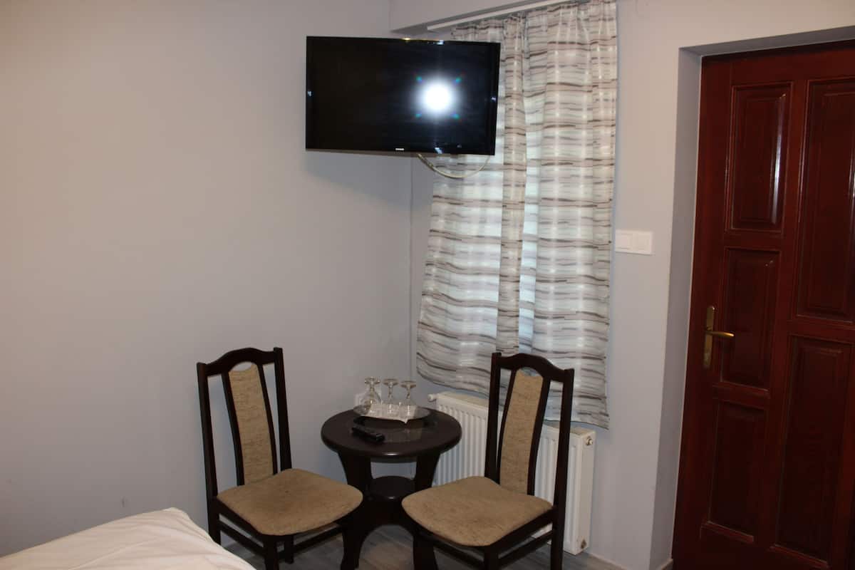 Une petite pièce avec un téléviseur fixé au mur, deux chaises, une petite table avec un plateau et des verres, et une porte.