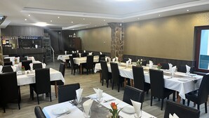 A restaurant with multiple tables set for dining, featuring white tablecloths and black chairs.